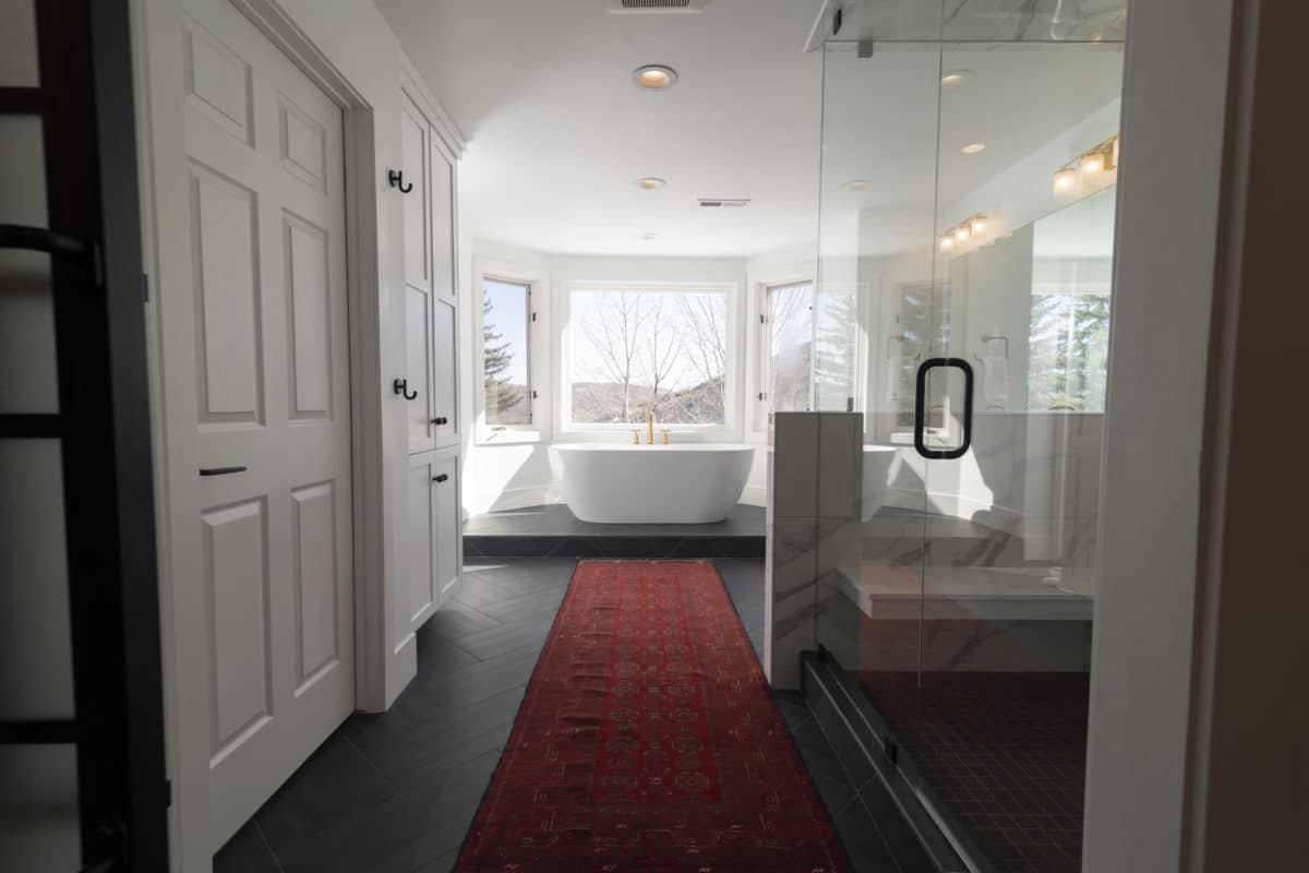 long view of a bathroom with tub on a platform surrounded by windows. Glass enclosure of shower and red carpet down the center