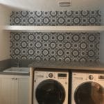 laundry room, washer and dryer with blue wallpaper behind and white shelf. white cabinets