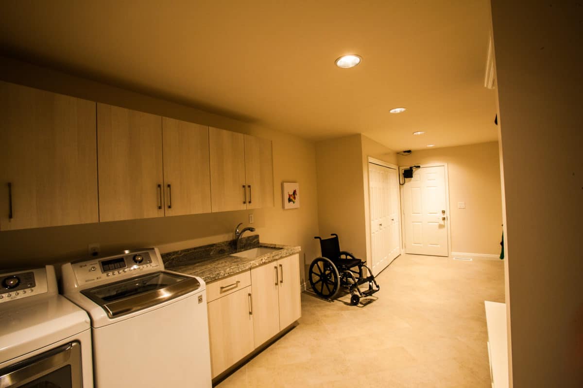 long laundry room exiting to the garage has a parking spot for a wheelchair and cabinetry for storage