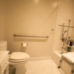 White tile in a Handicap accessible bathroom with grab bars and a shower seat