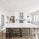 kitchen island with clear chairs, dark island with white counters and cabinets.