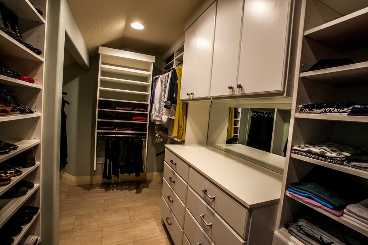 master closet with white cabinets and counter on right, and shelving unit on the far wall