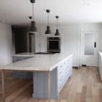 White kitchen with large kitchen island. wood floors and black pendant lights