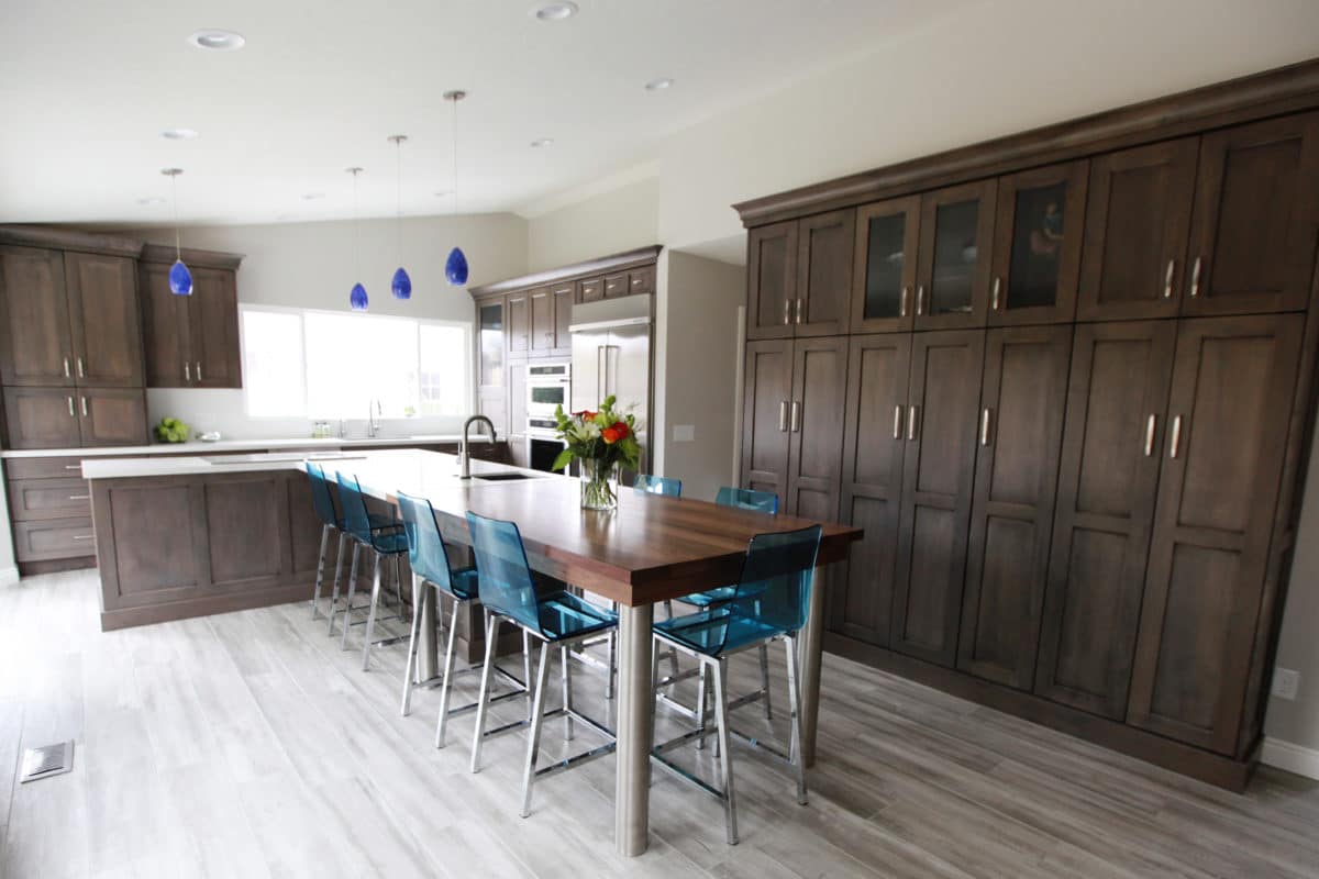 Blue chairs and blue pendants in this dark wood kitchen with integrated table and island