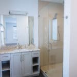 white vanity with open drawers and cabinet, glass enclosed shower and frameless mirror