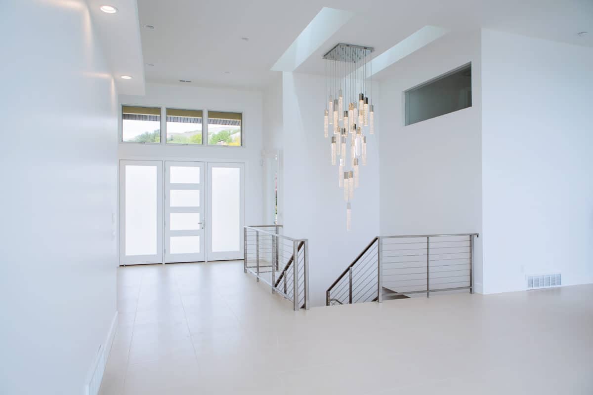 entry way of new custom home build, three pane door and stairs with metal railing. Chandelier, white walls and wood flooring