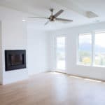 great room of new custom home fireplace with minimal hearth large ceiling fan, windows and door to outside and white paint