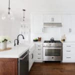 white kitchen cabinets with globe pendant lights over bar, black faucet with sink in island, stainless steel appliances wood flooring