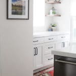 white kitchen cabinets with wood floating shelves above, stainless steel dishwasher