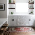 white kitchen cabinets with wood floating shelves around a window. wood floors
