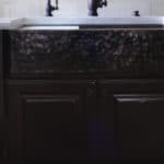 farmhouse sink with dark faucet and cabinets