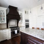 kitchen with oven and microwave built in, dark wood hood and island cabinets, white wall cabinets