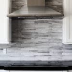 stack style tile backsplash and stainless vent hood white cabinets with dark countertop