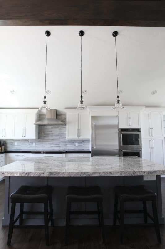 shaker style cabinets in white and dark island cabinets pendant lights in kitchen. Single door fridge and double wall ovens