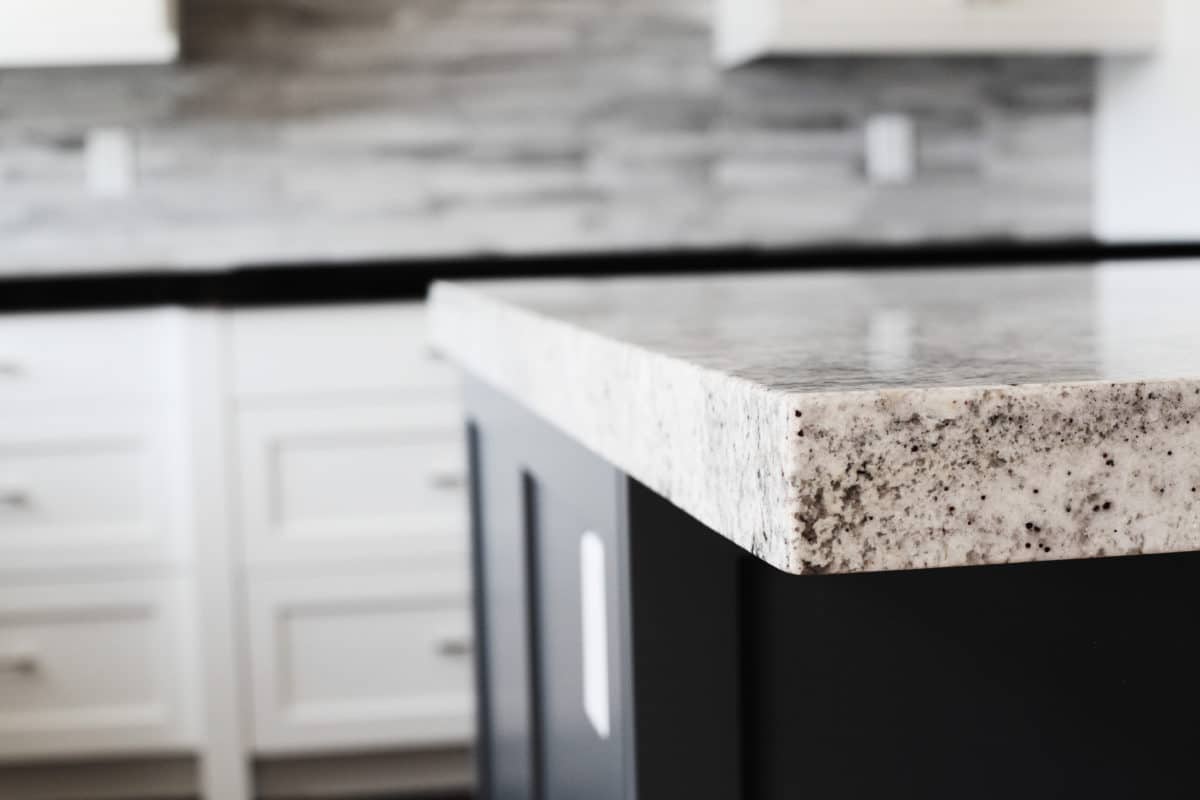 close up visual of light colored countertop dark island and white shaker cabinets, stack style tile backsplash