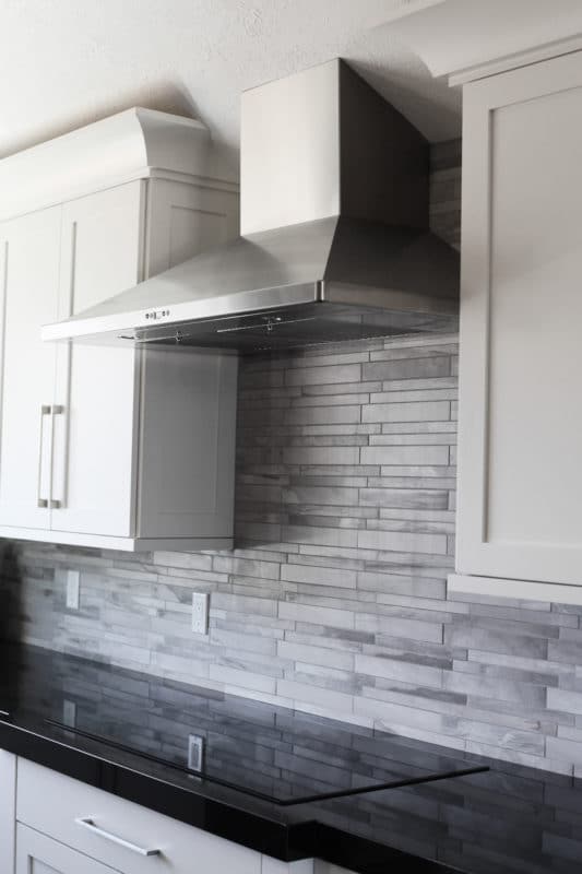stack style grout backsplash, stainless steel hood, white shaker cabinets and dark countertops