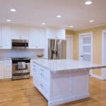 White L shaped kitchen with island, stainless appliances, yellow wall paint, white shaker style cabinets