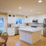 White L shaped kitchen with island, stainless appliances, yellow wall paint, white shaker style cabinets