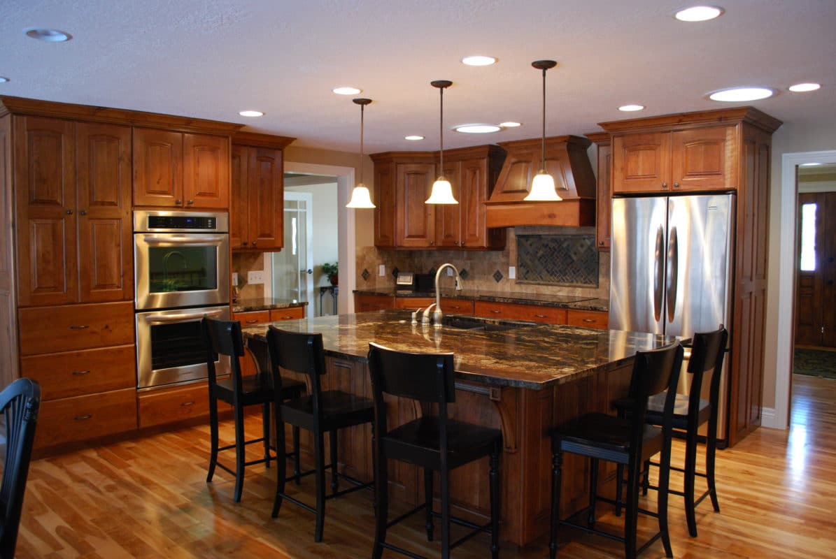 remodeled kitchen, hardwood floor, wall ovens, pendant lights, wood cabinets dark countertops. island with barstools