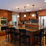 remodeled kitchen, hardwood floor, wall ovens, pendant lights, wood cabinets dark countertops. island with barstools