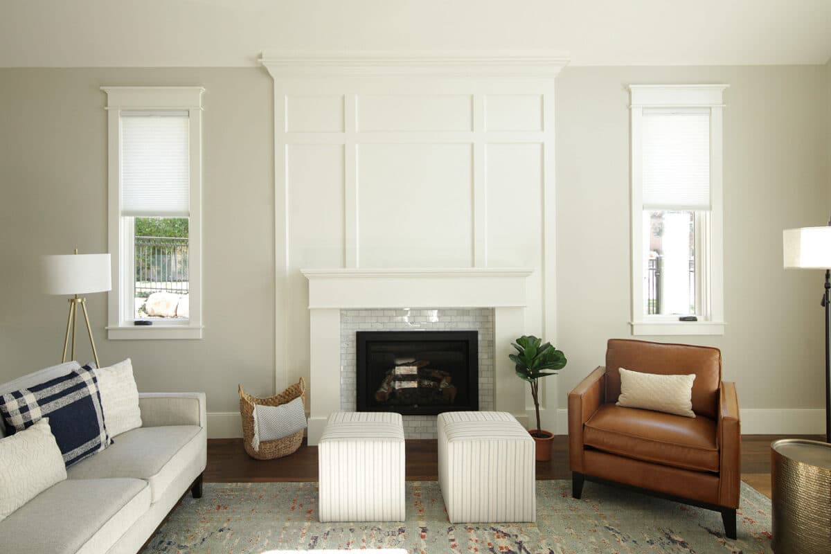 family room with fireplace flanked by two windows. wood detail above fireplace, symmetrical placement of furniture. white fireplace accent, beige walls and leather chair