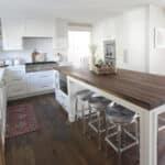 kitchen with integrated table and island. bar stools white kitchen cabinets wood countertop wood flooring