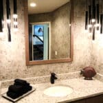 Modern bathroom remodel with wallpaper, black hanging lighting and a large wood framed mirror