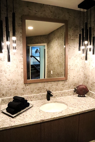 Modern bathroom remodel with wallpaper, black hanging lighting and a large wood framed mirror