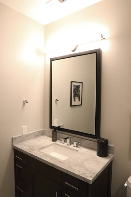 Contemporary bathroom vanity with marble countertops, bright lighting, and dark wood cabinets