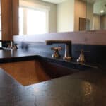 Modern bathroom design with dark stone countertop, copper lined sink and dual vanity with large natural wood framed mirror