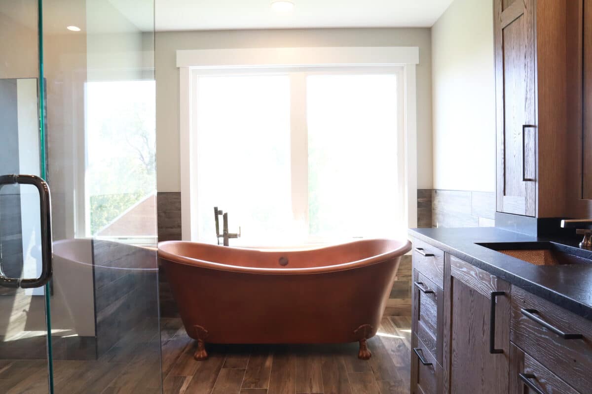 Unique and luxurious copper claw-foot bathtub in remodeled bathroom with natural wood flooring and cabinets