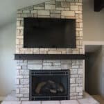 Front view of custom stone fireplace with iron mantel and mounted TV above fireplace by Fine Remodel