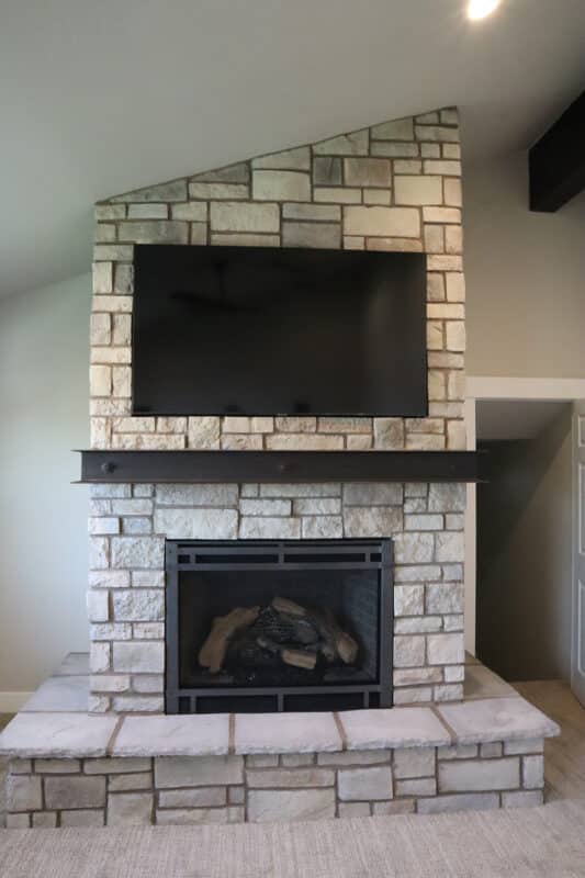 Front view of custom stone fireplace with iron mantel and mounted TV above fireplace by Fine Remodel