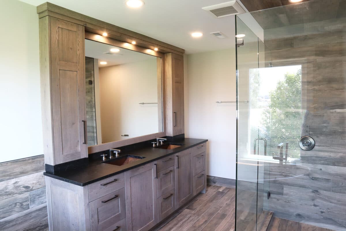 Modern bathroom design with dark stone countertop, copper lined sink, dual vanity, and large natural wood framed mirror and cabinets