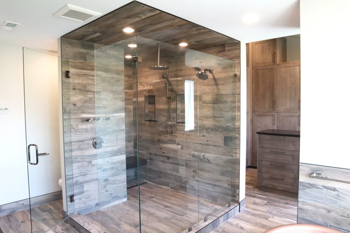 Custom modern walk-in shower with multiple recessed lighting, shower heads, benched seating, custom shelving, and natural wood flooring and paneling.