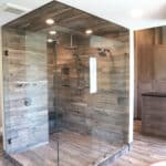 Custom modern walk-in shower with multiple recessed lighting, shower heads, benched seating, custom shelving, and natural wood flooring and paneling.