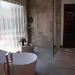 High-end residential bathroom new build. Modern marble walk-in shower, freestanding bathtub, and seamless flooring